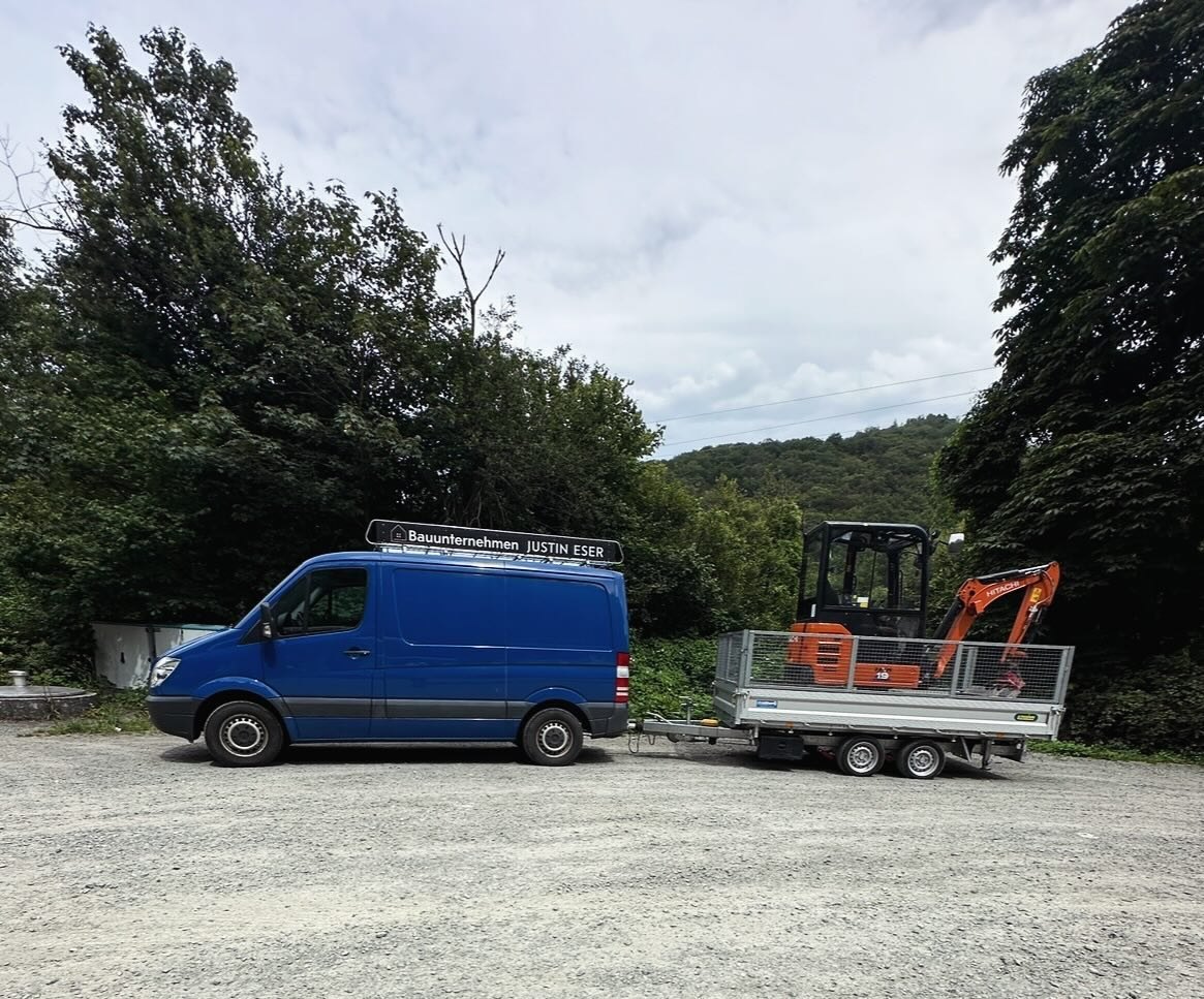 Firmentransporter mit Dachschild „Bauunternehmen Justin Eser“ und Anhänger mit Minibagger